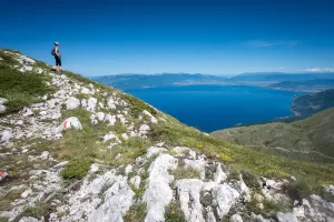 a hiker standing on a mountain top slope overlooking a lake