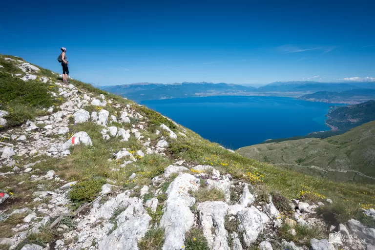 a hiker standing on a mountain top slope overlooking a lake