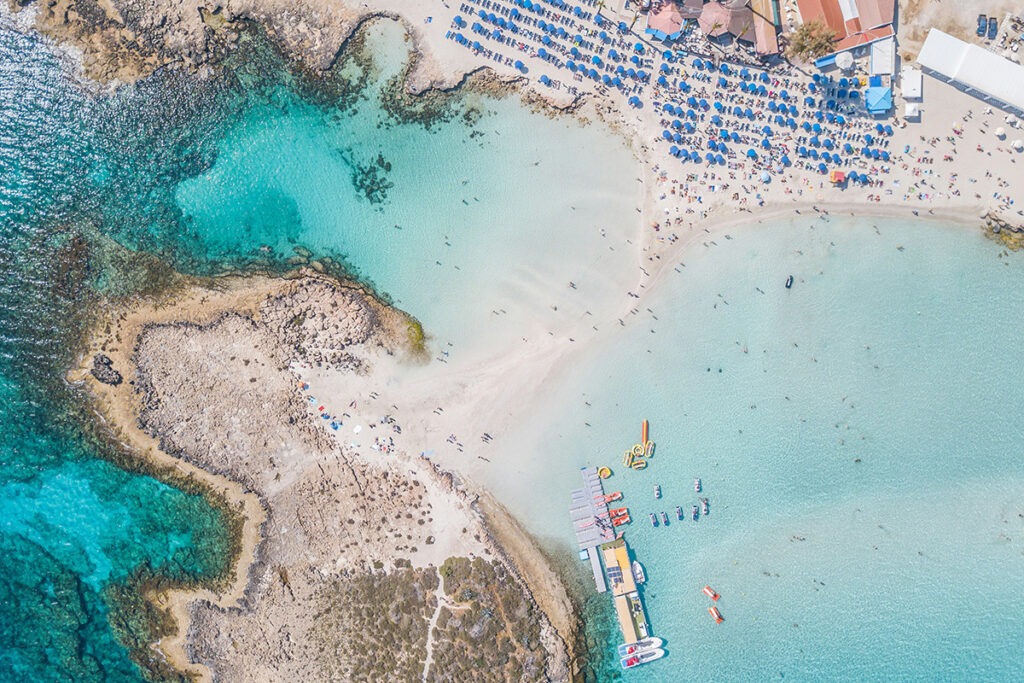 High aerial view of a beach with umbrellas and surounding coastal water and lansdcapes at Ayia Napa Cyprus