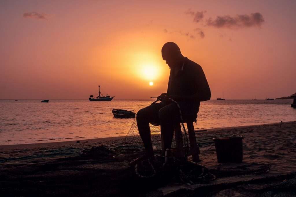 silhouette of a man sitting on a chair near a body of water during sunset