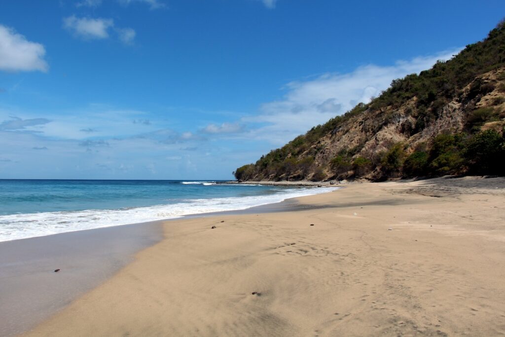 a sandy beach with blue water and blue sky